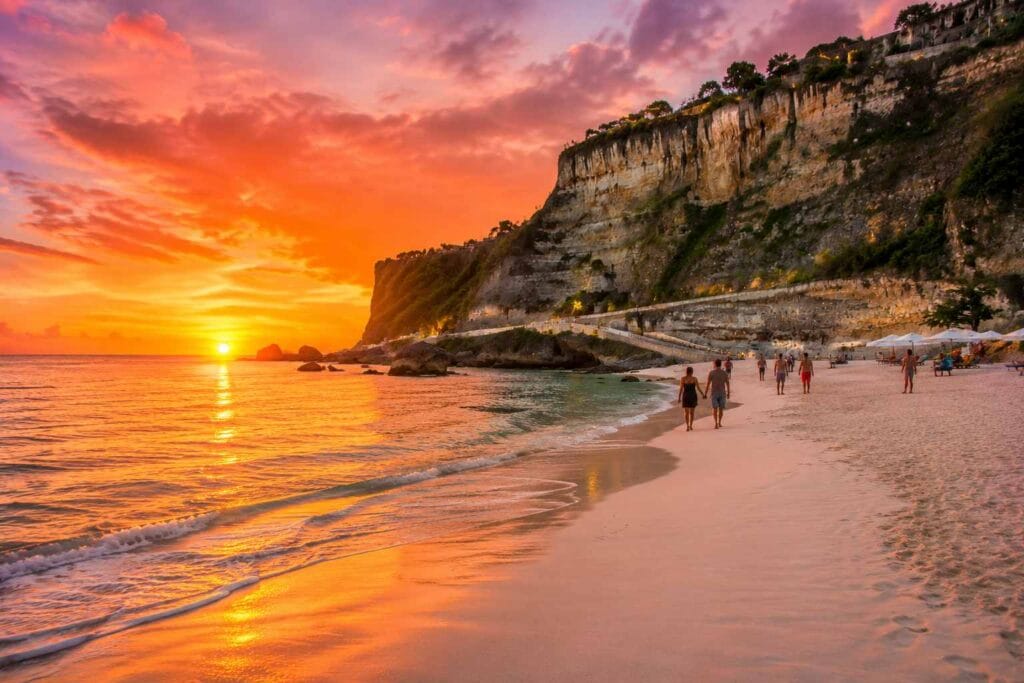 Visitors walking along Melasti Beach Bali during a beautiful sunset with orange sky and coastal cliffs